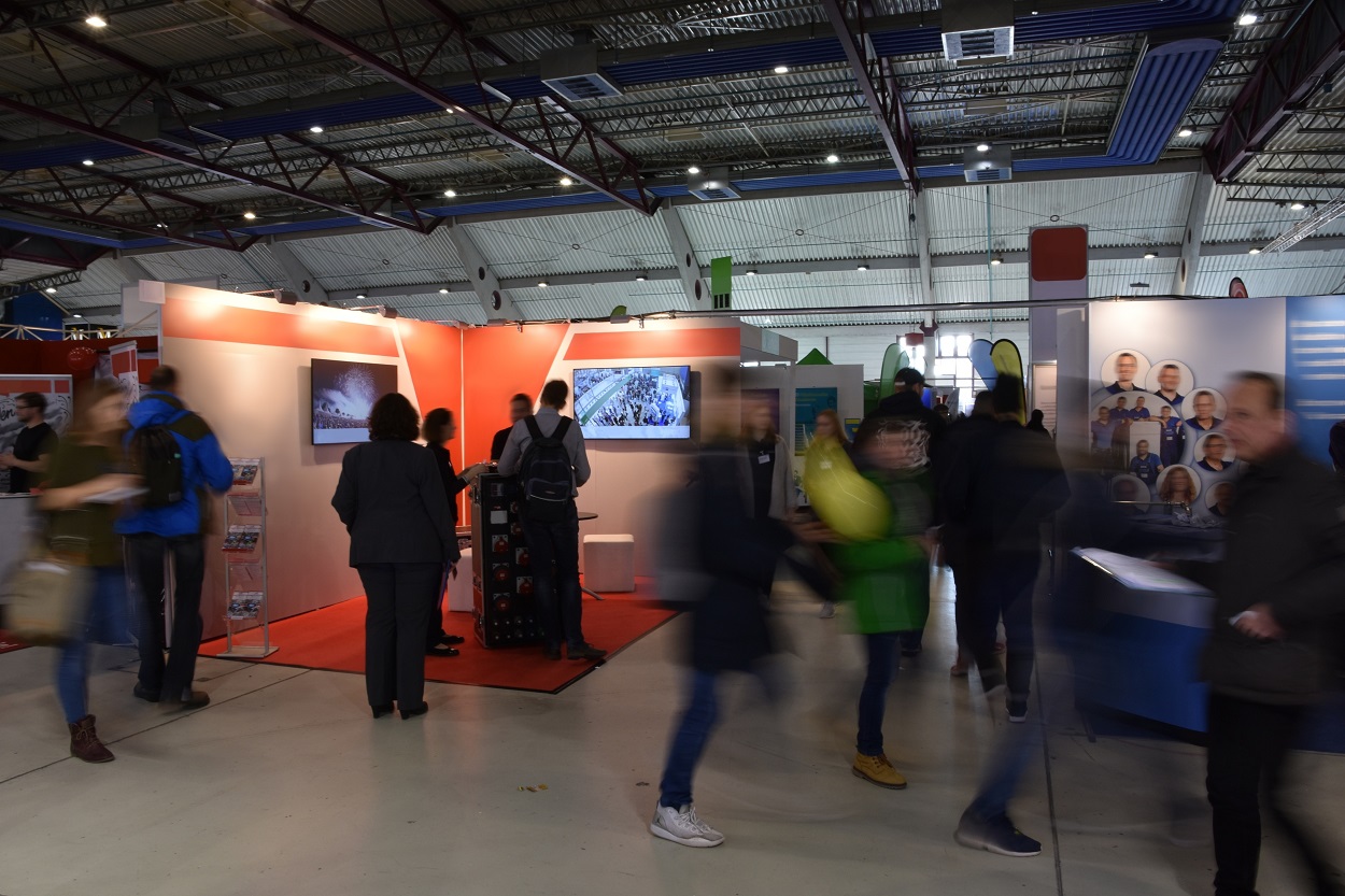 Dynamiczna hala targowa, gdzie błędy w projektowaniu stoiska targowego sprawiają, że potencjalni klienci przechodzą obok obojętnie.